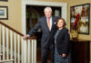 President Underwood leads Mercer for nearly 20 transformative years President William D. Underwood and wife Lesli Underwood stand together beside a staircase in a well-decorated home interior.