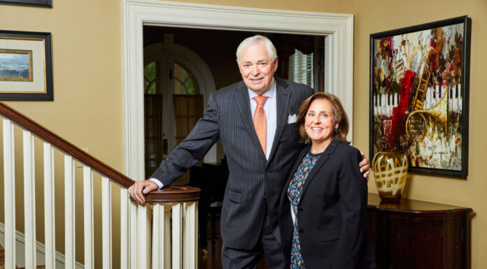 President Underwood leads Mercer for nearly 20 transformative years President William D. Underwood and wife Lesli Underwood stand together beside a staircase in a well-decorated home interior.