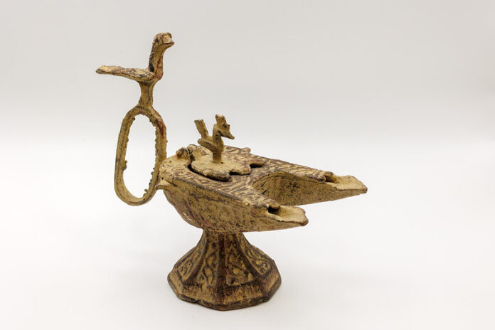 250722MUArtifacts_0224-L An ornate, ancient bronze oil lamp with animal-shaped decorations on a plain white background.