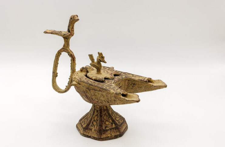An ornate, ancient bronze oil lamp with animal-shaped decorations on a plain white background.