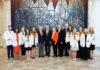 School of Medicine announces 2025 Nathan Deal Scholars A group of people in white coats and formal attire pose in front of a large stained glass window indoors.