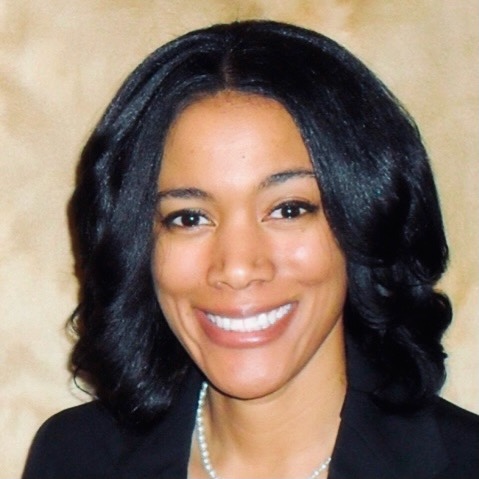 A woman with shoulder-length black hair smiles at the camera, wearing a black blazer and a pearl necklace.