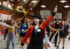 MU Miracle helps local families while giving students purpose A group of people dance indoors as a person in a red jacket and top hat leads with an arm raised.