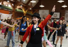 MU Miracle helps local families while giving students purpose A group of people dance indoors as a person in a red jacket and top hat leads with an arm raised.