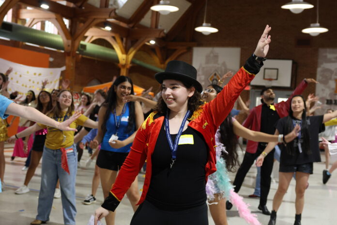 HaileyDance A group of people dance indoors as a person in a red jacket and top hat leads with an arm raised.