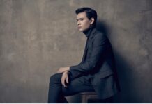 McDuffie Center for Strings welcomes new distinguished artist Stefan Jackiw A man in a dark suit sits sideways on a stool against a textured gray wall, looking ahead with a neutral expression.