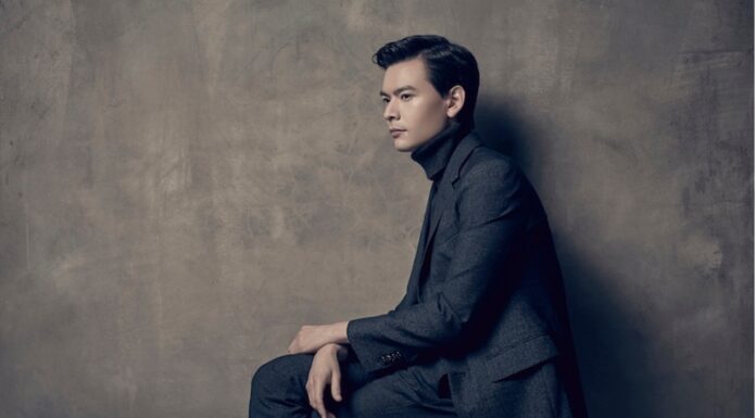 McDuffie Center for Strings welcomes new distinguished artist Stefan Jackiw A man in a dark suit sits sideways on a stool against a textured gray wall, looking ahead with a neutral expression.