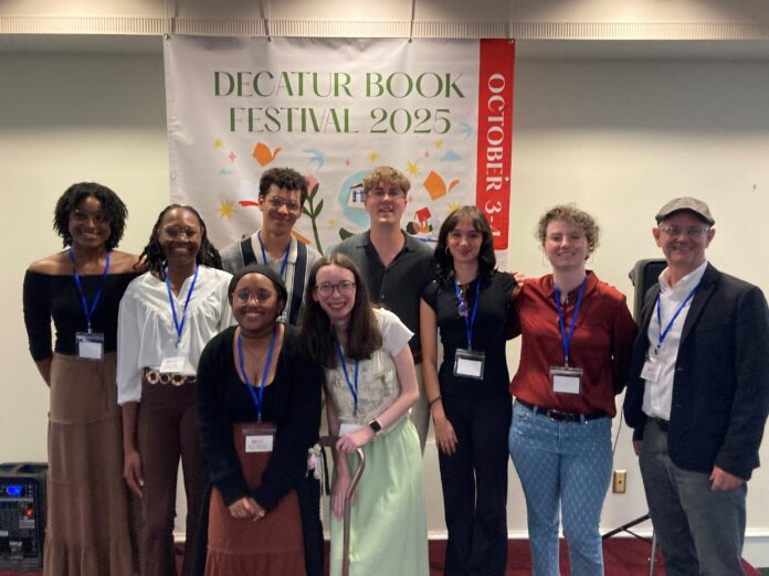 book fest group Eight young adults and and a professor stand in front of a Decatur Book Festival 2025 banner, smiling at the camera.
