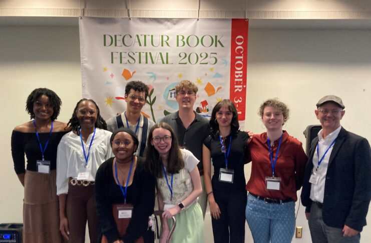 Eight young adults and and a professor stand in front of a Decatur Book Festival 2025 banner, smiling at the camera.