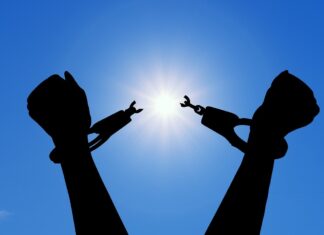 Release is a gift you can give yourself | Dr. Craig McMahan Silhouette of hands breaking free from handcuffs against a bright sun in a clear blue sky.