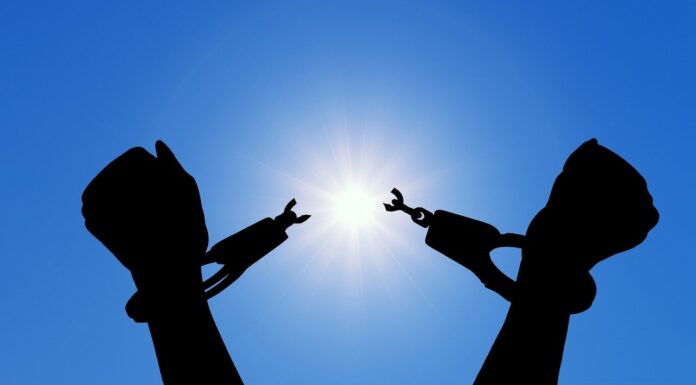 Release is a gift you can give yourself | Dr. Craig McMahan Silhouette of hands breaking free from handcuffs against a bright sun in a clear blue sky.