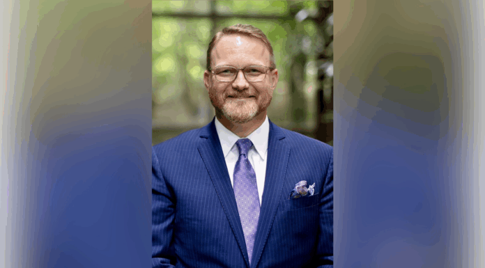 Dr. Michael Crouch appointed dean of College of Pharmacy A man wearing glasses, a blue suit, and a purple tie stands indoors, smiling at the camera.