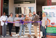 KidsABC celebrates Bleckley hospital’s emergency department for pediatric care Seven people stand behind a purple ribbon at an outdoor event in front of a building, with a kids ABC banner displayed.