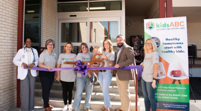 KidsABC celebrates Bleckley hospital’s emergency department for pediatric care Seven people stand behind a purple ribbon at an outdoor event in front of a building, with a kids ABC banner displayed.