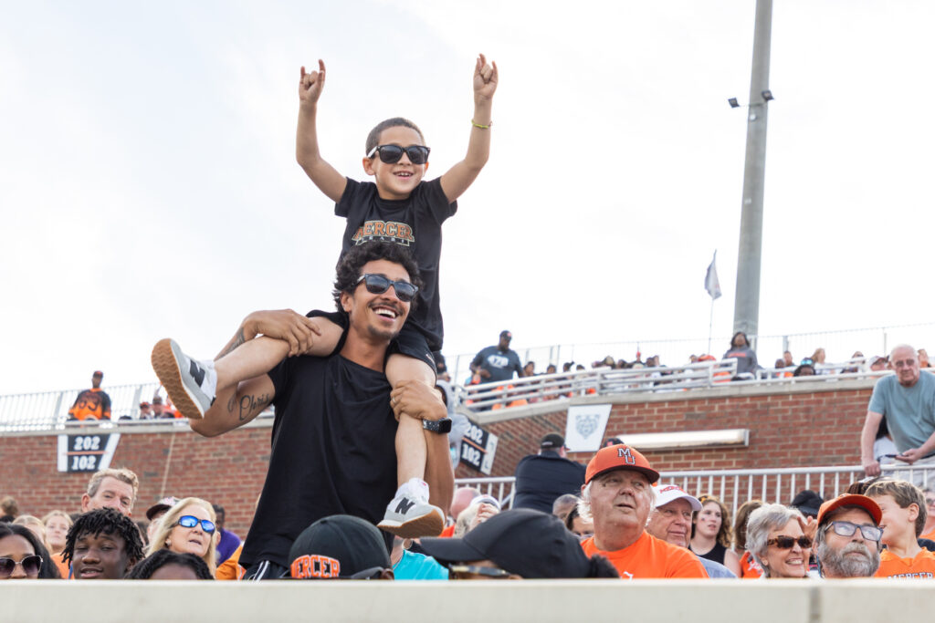 A man with a child on his shoulders cheers in Five Star Stadium.