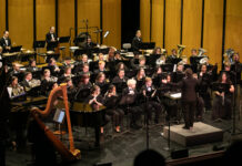 Mercer Wind Ensemble presents ‘Voices’ at The Grand on Nov. 24 A conductor leads a large orchestra of musicians playing various instruments on a concert hall stage.
