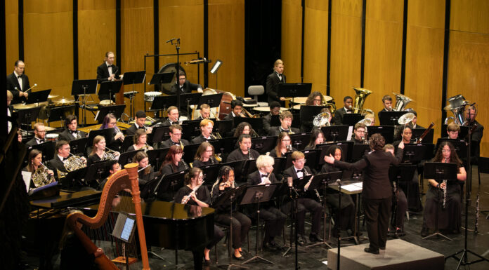 Mercer Wind Ensemble presents ‘Voices’ at The Grand on Nov. 24 A conductor leads a large orchestra of musicians playing various instruments on a concert hall stage.