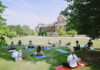 Mercer’s mindfulness club helps students learn meditation, yoga A group of people practice yoga on mats in a grassy area near a large brick building on a sunny day.