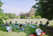 Mercer’s mindfulness club helps students learn meditation, yoga A group of people practice yoga on mats in a grassy area near a large brick building on a sunny day.