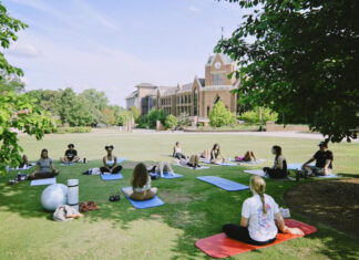 Mercer’s mindfulness club helps students learn meditation, yoga A group of people practice yoga on mats in a grassy area near a large brick building on a sunny day.