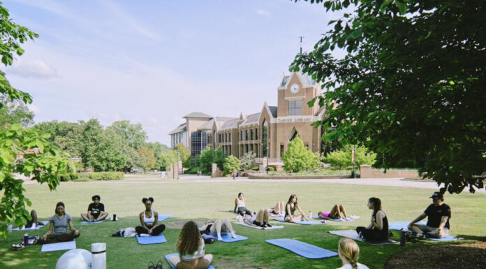 Mercer’s mindfulness club helps students learn meditation, yoga A group of people practice yoga on mats in a grassy area near a large brick building on a sunny day.