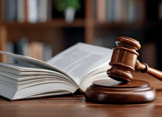 From the bench to the classroom: How judges enhance legal education at Mercer Law A wooden judge’s gavel rests on a sound block next to an open book on a wooden table, with shelves in the background.