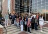 Biology professor recognized for student mentorship initiatives A group of students poses on outdoor steps in front of a modern building with large glass windows at dusk.