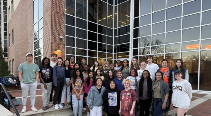 Biology professor recognized for student mentorship initiatives A group of students poses on outdoor steps in front of a modern building with large glass windows at dusk.