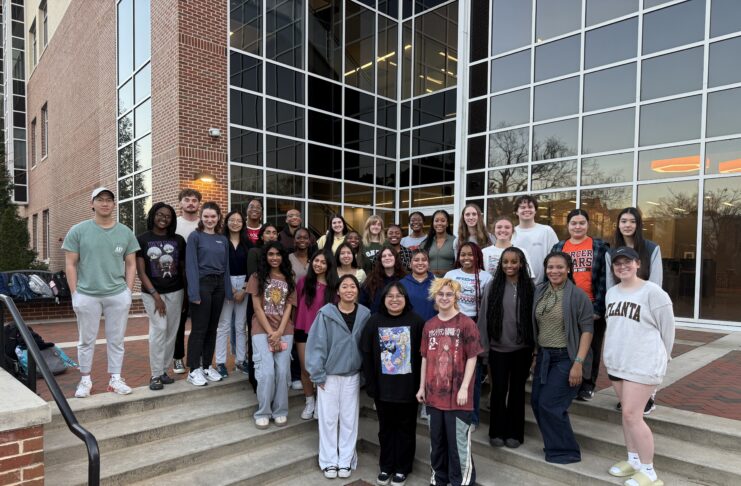 A group of students poses on outdoor steps in front of a modern building with large glass windows at dusk.