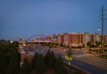 Mercer marketing wins ‘Best of’ awards for writing, video A street scene at dusk shows a pedestrian bridge, modern buildings, and trees, with streetlights and sparse traffic.