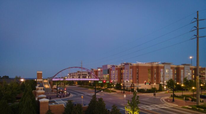 Mercer marketing wins ‘Best of’ awards for writing, video A street scene at dusk shows a pedestrian bridge, modern buildings, and trees, with streetlights and sparse traffic.