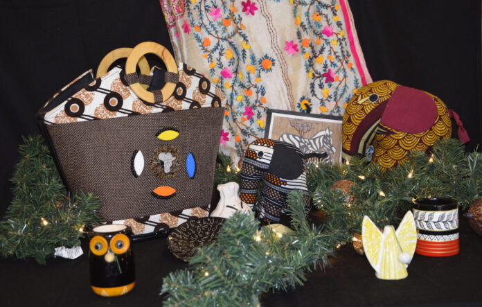 Display of handmade crafts including bags, mugs, fabric animals, and greenery with a patterned cloth backdrop.