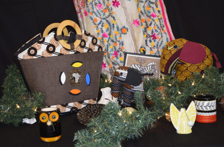 Display of handmade crafts including bags, mugs, fabric animals, and greenery with a patterned cloth backdrop.