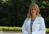 Dr. Nicole Metzger named 2025 American College of Clinical Pharmacy fellow Woman in a white lab coat standing outdoors with trees and greenery in the background.