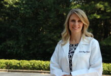 Dr. Nicole Metzger named 2025 American College of Clinical Pharmacy fellow Woman in a white lab coat standing outdoors with trees and greenery in the background.