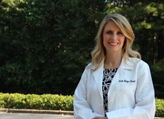 Dr. Nicole Metzger named 2025 American College of Clinical Pharmacy fellow Woman in a white lab coat standing outdoors with trees and greenery in the background.