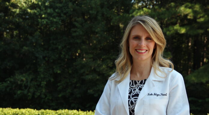 Dr. Nicole Metzger named 2025 American College of Clinical Pharmacy fellow Woman in a white lab coat standing outdoors with trees and greenery in the background.