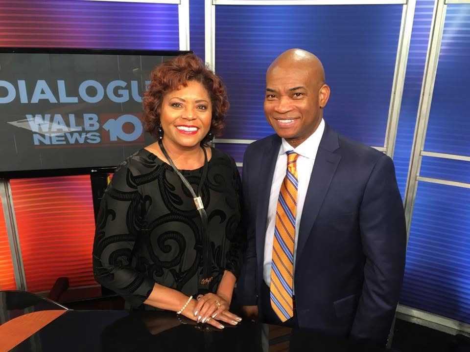 Two news anchors stand together in a TV studio in front of a WALB News 10 and Dialogue sign.
