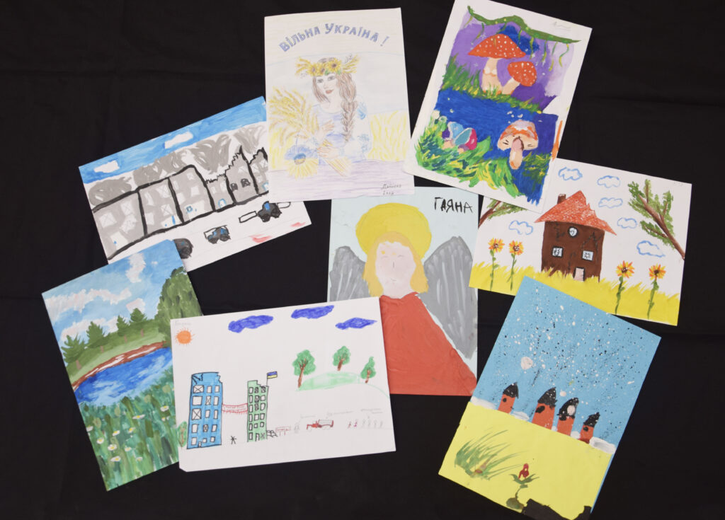 Nine colorful childrens drawings featuring houses, nature, angels, sunflowers, mushrooms, and a Ukrainian flag.