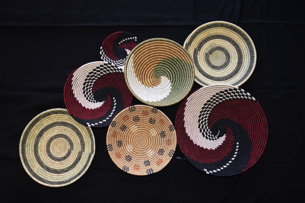 Seven woven baskets with intricate spiral and geometric patterns are arranged on a black background.