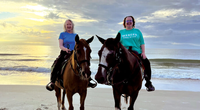Discovering her calling: How Professor Margie Alsbrook’s journey led to Mercer Law Two women riding horses on a sandy beach with the ocean and a cloudy sky in the background at sunset.