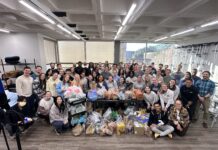 Mercer campus pantries support Bears in need A large group of people poses indoors around tables filled with assorted bags and boxes of donated goods.