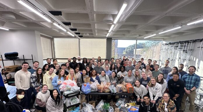 Mercer campus pantries support Bears in need A large group of people poses indoors around tables filled with assorted bags and boxes of donated goods.