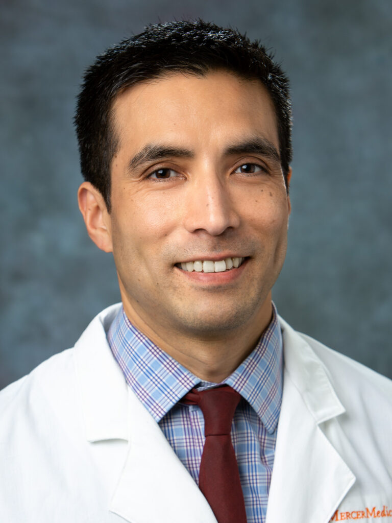 Dr. Rafael Ponce-Terashima in a white lab coat and tie smiling in front of a neutral gray background.