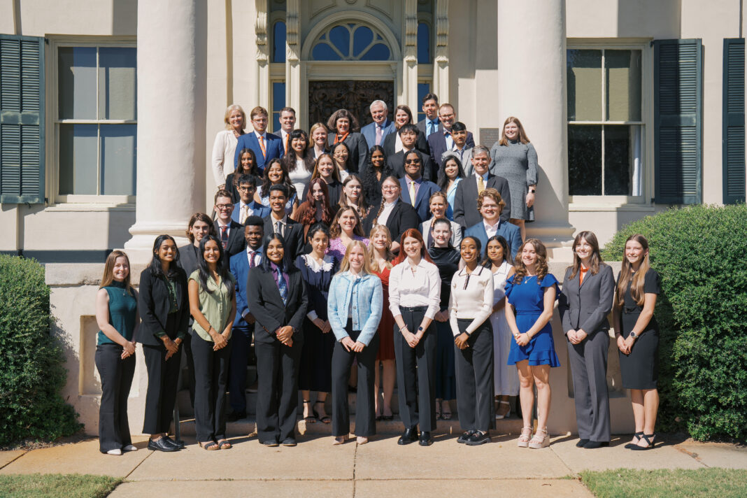 A large group of people in formal attire poses for a group photo on steps outside a building with columns.