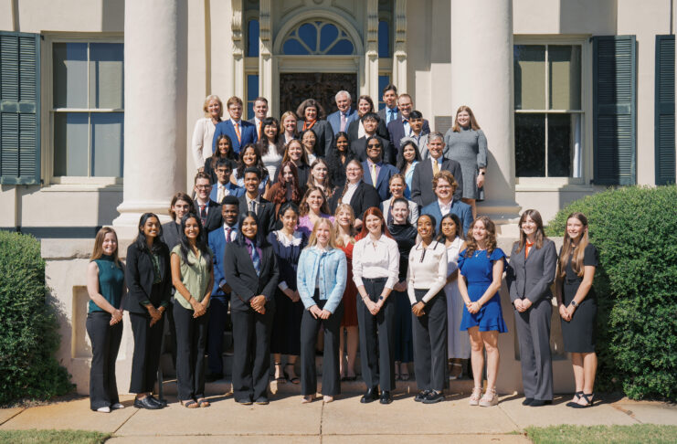 A large group of people in formal attire poses for a group photo on steps outside a building with columns.