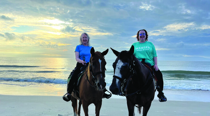 Discovering her calling: How Professor Margie Alsbrook’s journey led to Mercer Law Two women riding horses on a sandy beach with the ocean and a cloudy sky in the background at sunset.