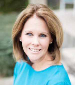 Woman with shoulder-length light brown hair, wearing a blue top, smiling at the camera outdoors.