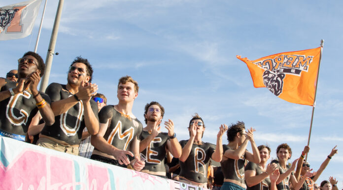 3 things to know about Mercer’s playoff game vs. South Dakota: Dec. 6, 2025 A group of fans with painted chests stands in a row cheering, while one holds an orange flag with a bear logo.
