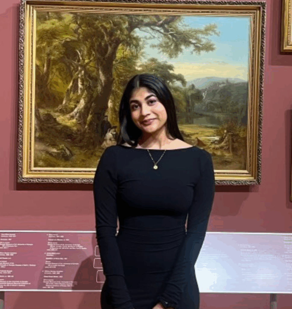 Woman in a black dress stands in front of a framed landscape painting in an art gallery.